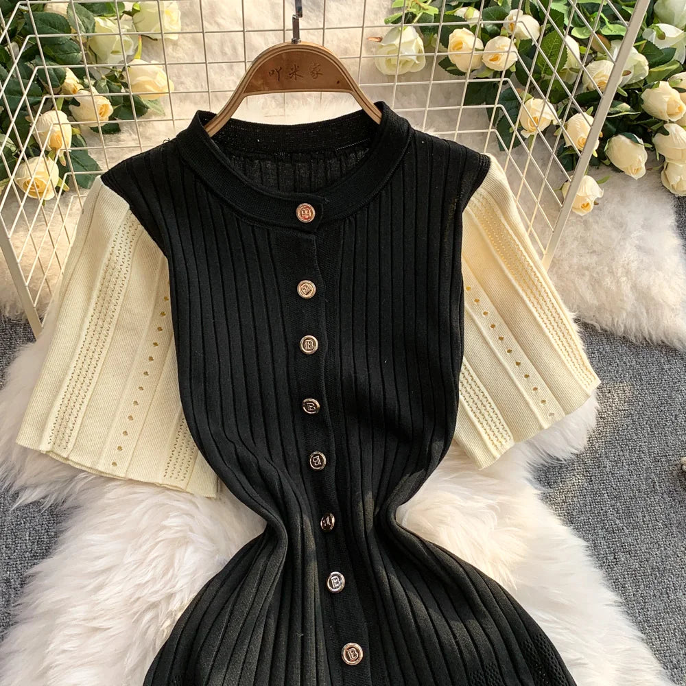 Black ribbed dress with buttons on a hanger against a decorative background with flowers and fabric.