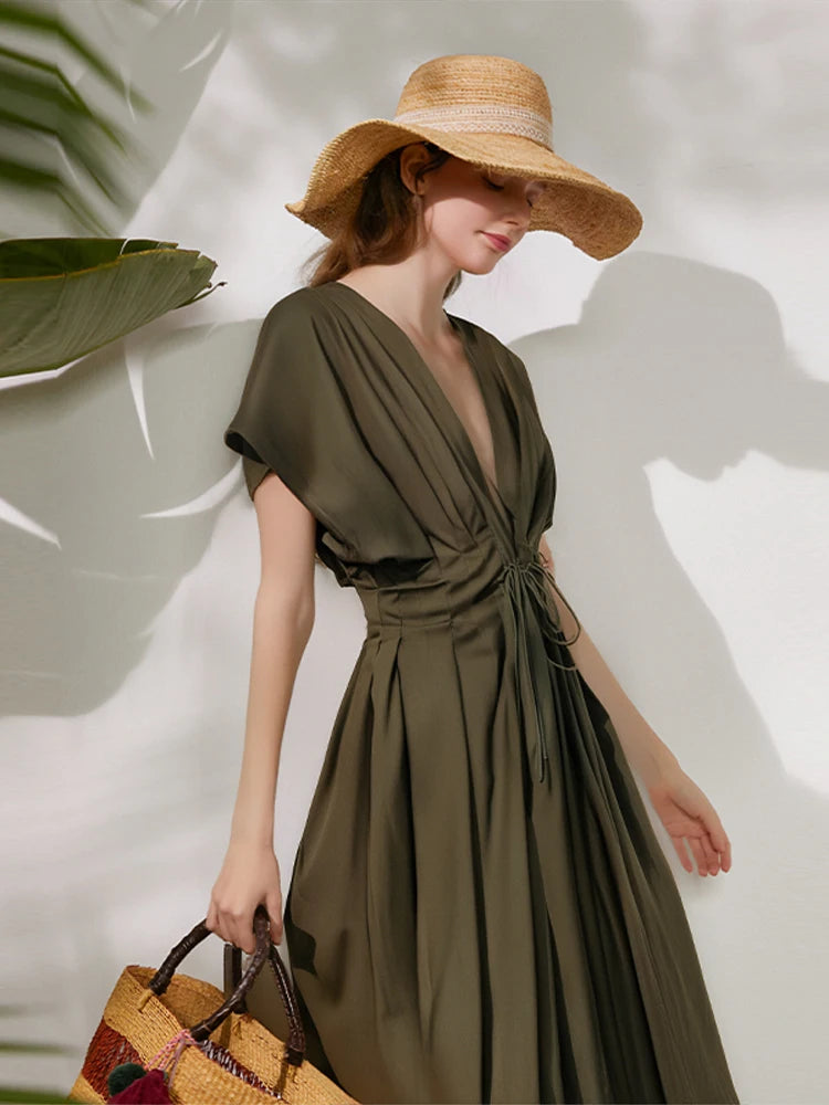 Woman wearing an olive green dress and wide-brimmed hat against a light background