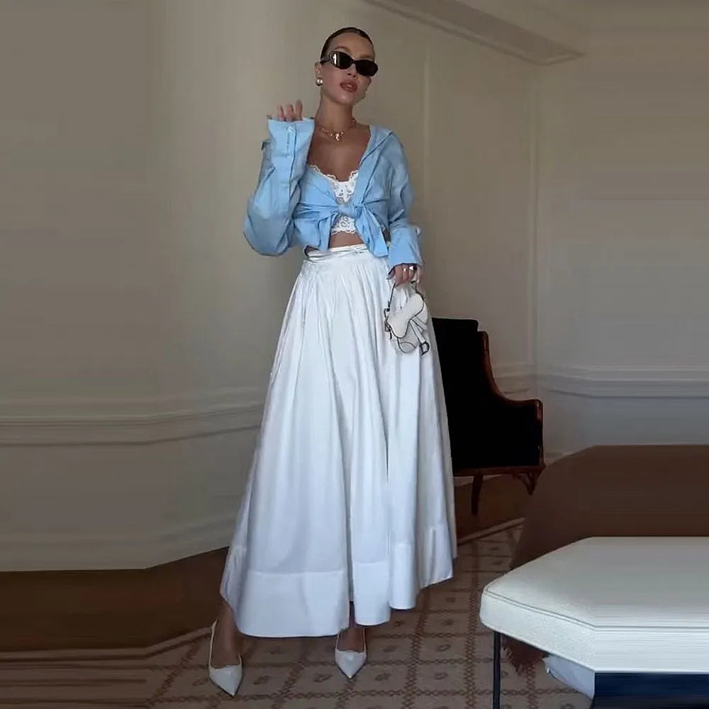 Woman in a stylish outfit with a light blue jacket and white skirt in an elegant room.