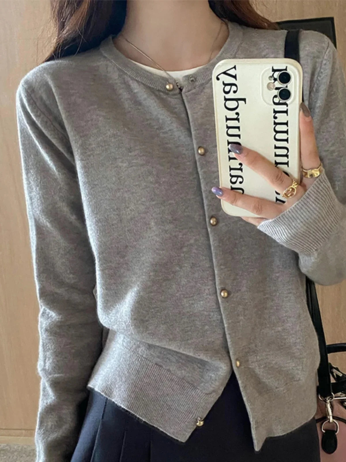 Person wearing a gray cardigan holding a phone with a visible brand logo.