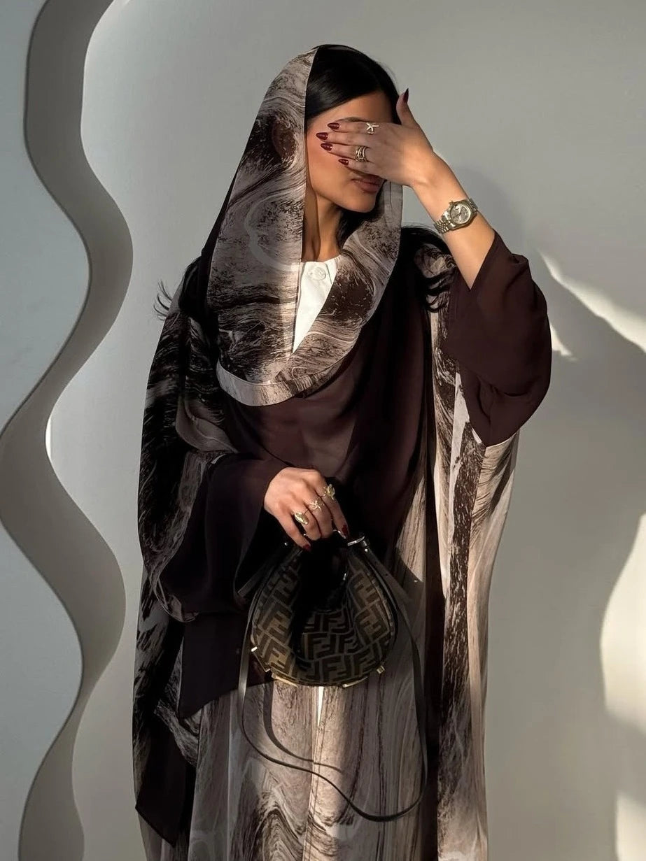 Woman wearing a dark abaya with a patterned scarf against a light gray background
