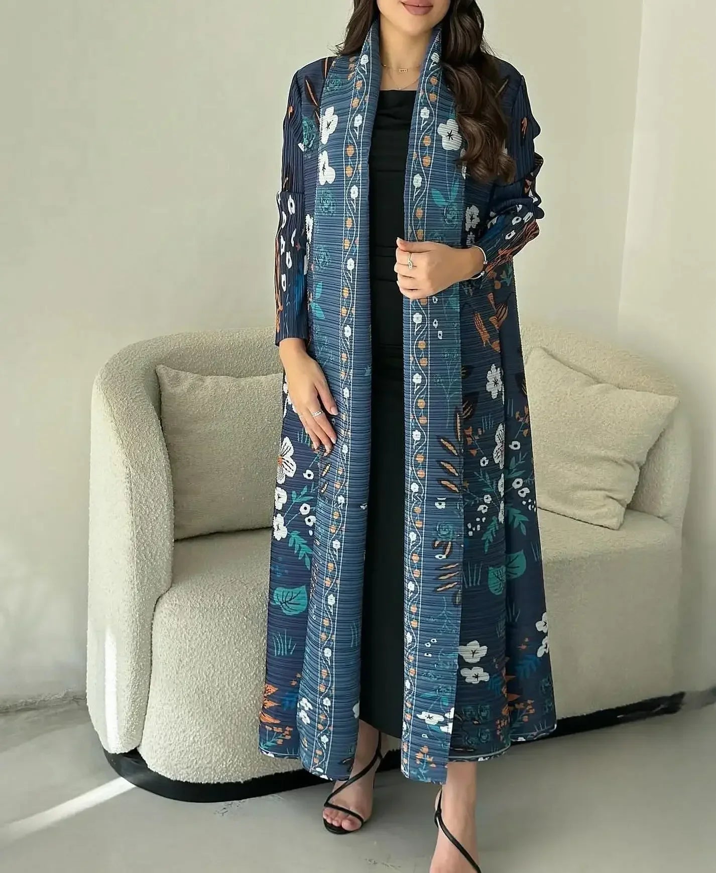 Woman wearing a long, floral-patterned blue coat in a minimalistic room.