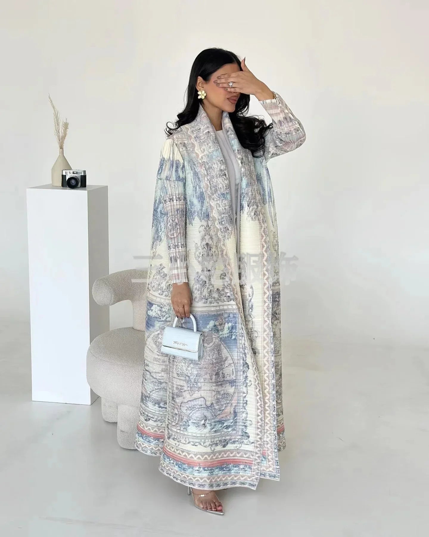 Woman wearing a long, patterned dress in a minimal white room.