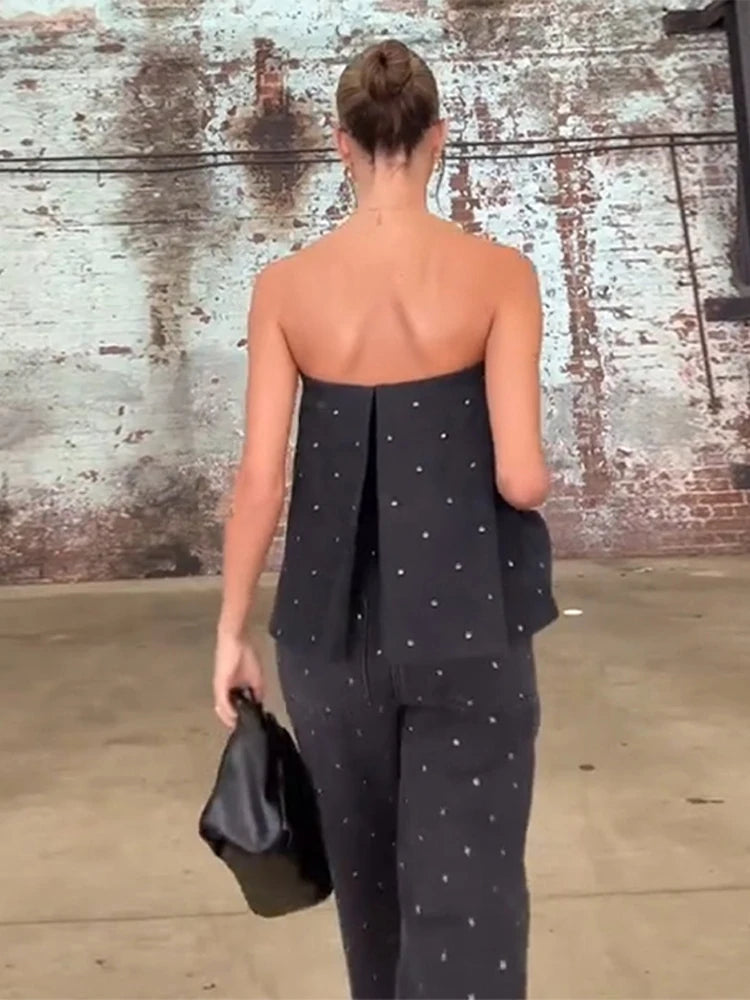 Woman wearing a strapless black jumpsuit with white polka dots against a textured wall.