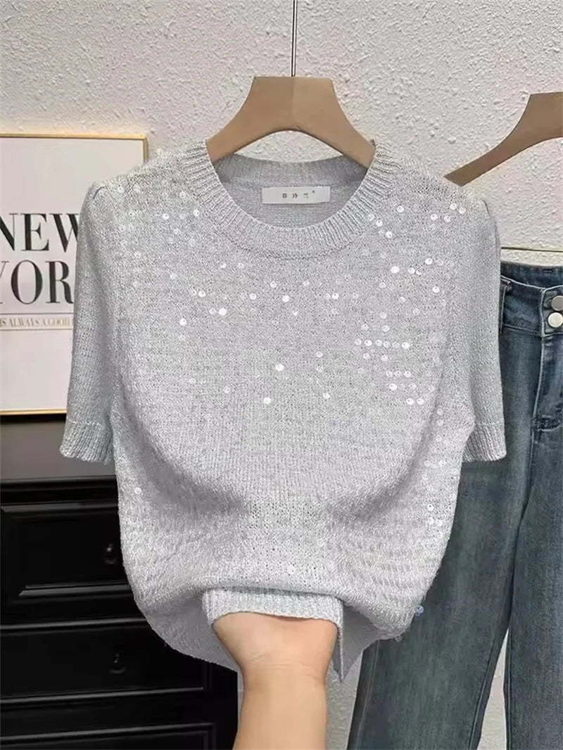 Gray sequin sweater on a hanger with jeans in the background