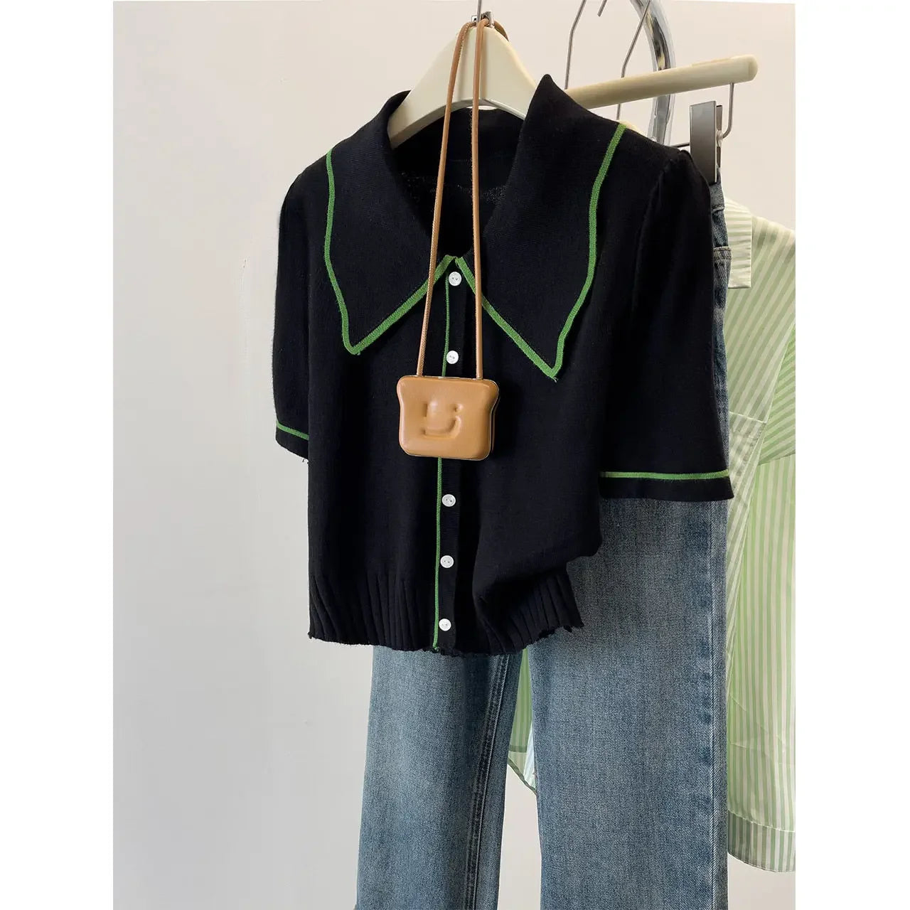 Black shirt with green trim and beige bag on a hanger against a neutral background