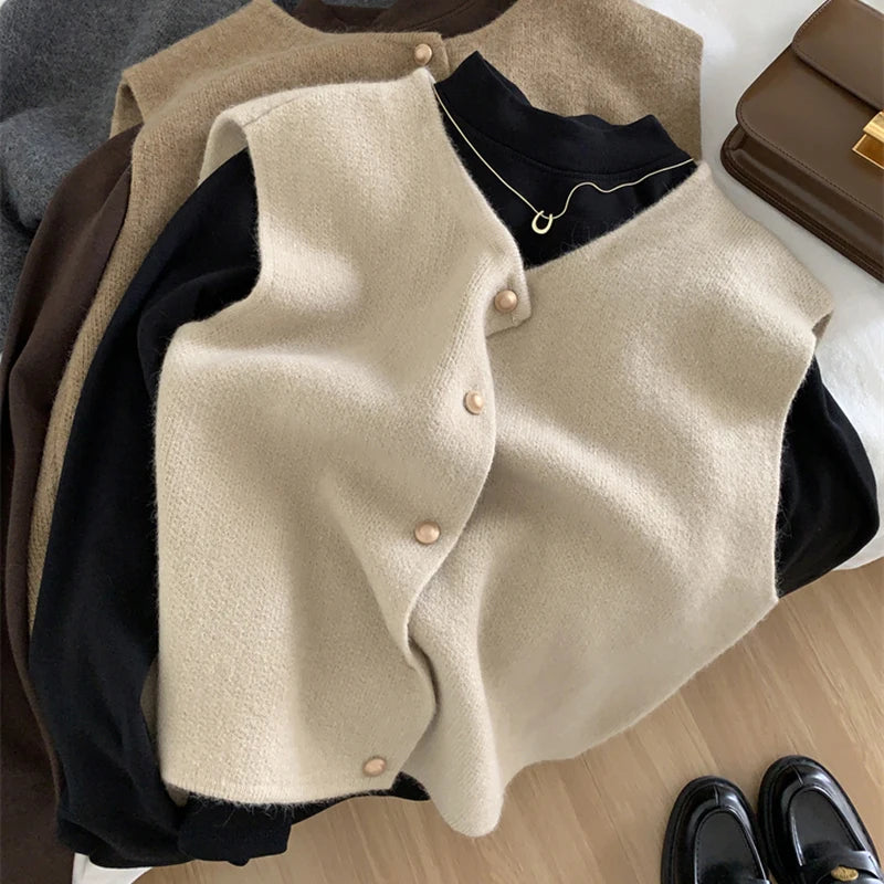 Beige cardigan over a black shirt with a necklace, on a wooden surface.
