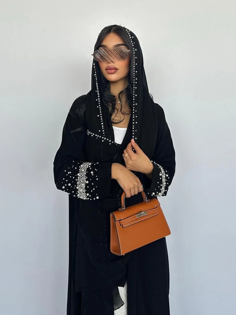Person wearing a black outfit with embellishments and holding a brown handbag against a white background
