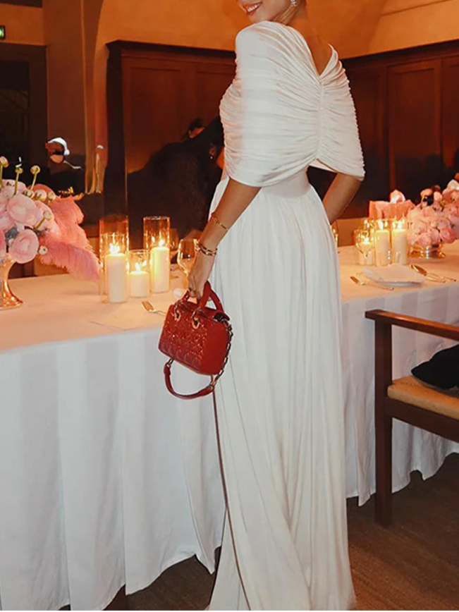 Woman in a white dress holding a red handbag in a decorated indoor setting with 'ZAHM' branding.