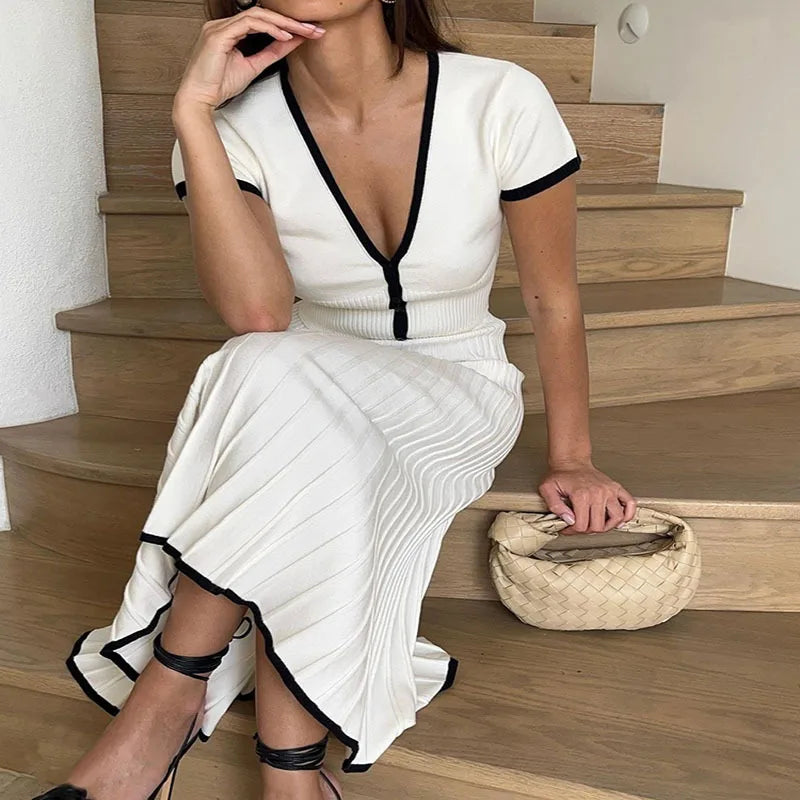 Woman in a white dress with black trim sitting on wooden stairs.