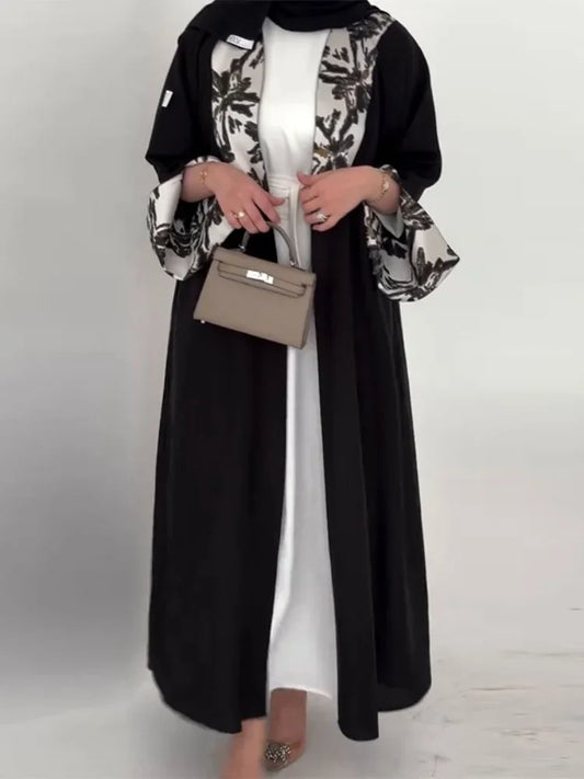 Woman wearing a black and floral abaya with a beige handbag on a white background