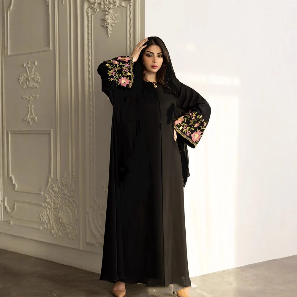 Woman wearing a black abaya with floral embroidery in a decorated room.