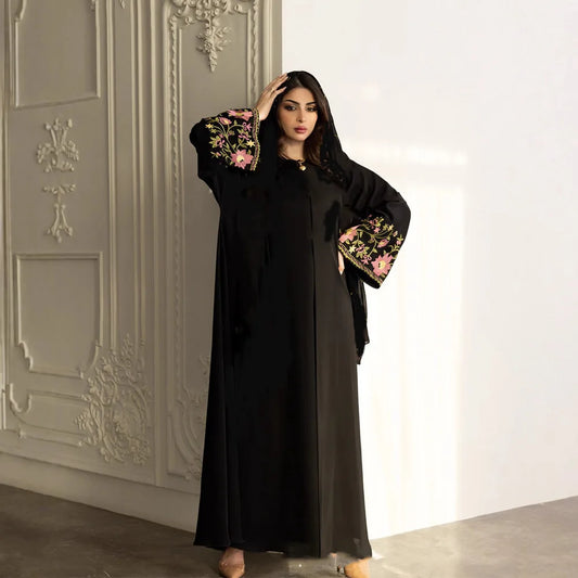 Woman wearing a black abaya with floral embroidery in a decorated room.