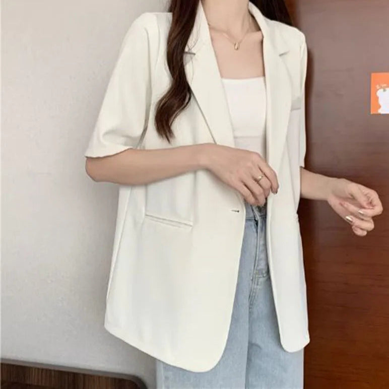 Person wearing a white blazer over a light blue top against a neutral background