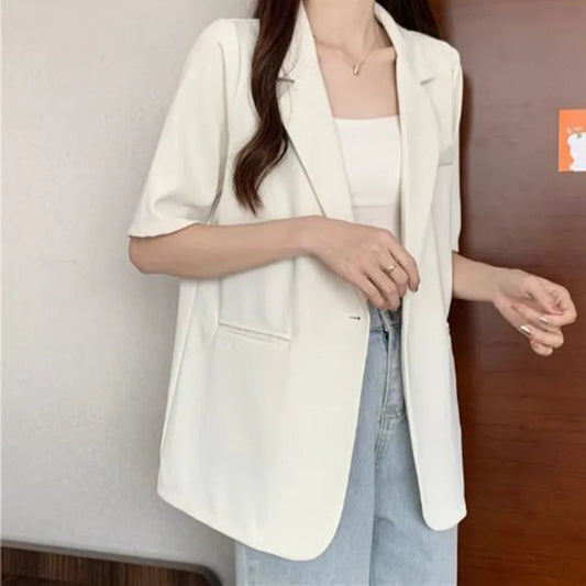 Person wearing a white blazer over a light blue top against a neutral background