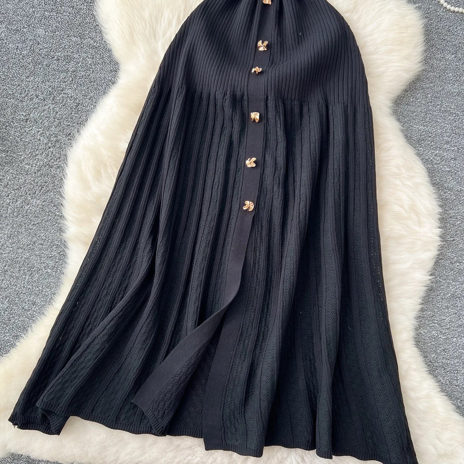 Black dress with gold buttons on a textured white and gray surface