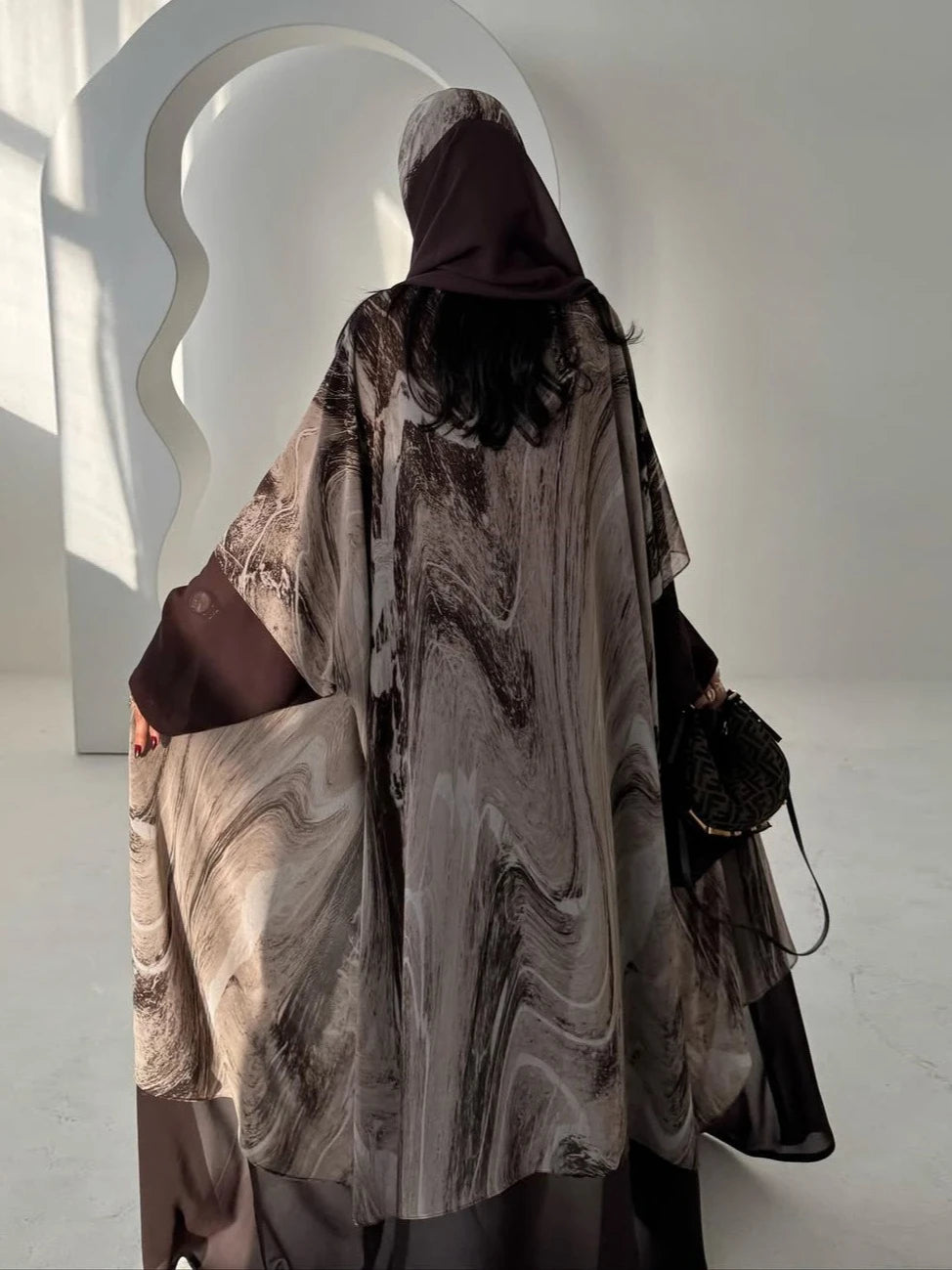 Person wearing a marble-patterned abaya in a minimalistic setting