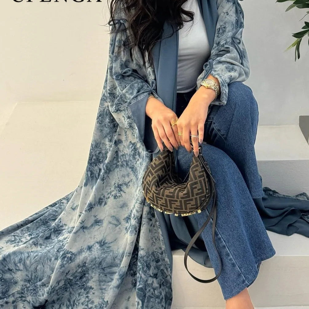 Person wearing a blue floral coat and jeans, holding a handbag with a brand logo.