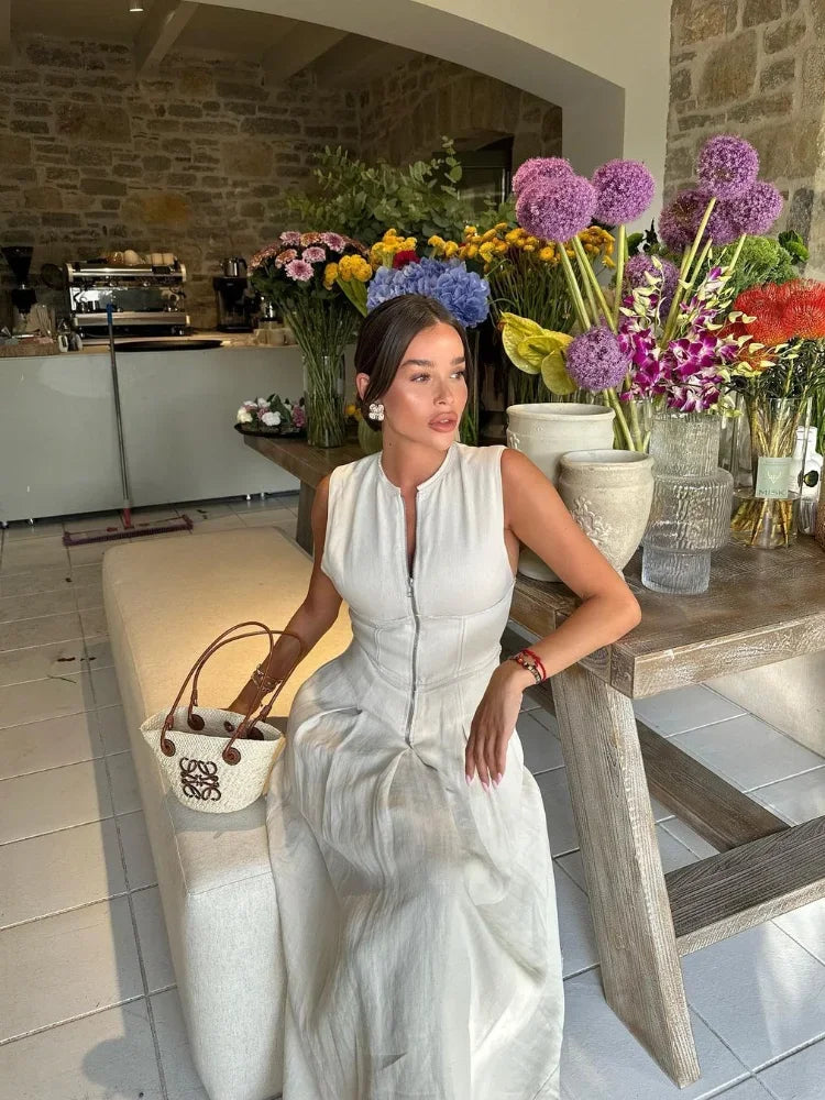 Woman in a white dress sitting at a table with flowers in a rustic kitchen.