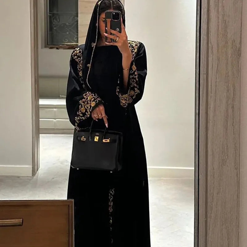 Person wearing a black outfit with gold embroidery holding a black handbag.