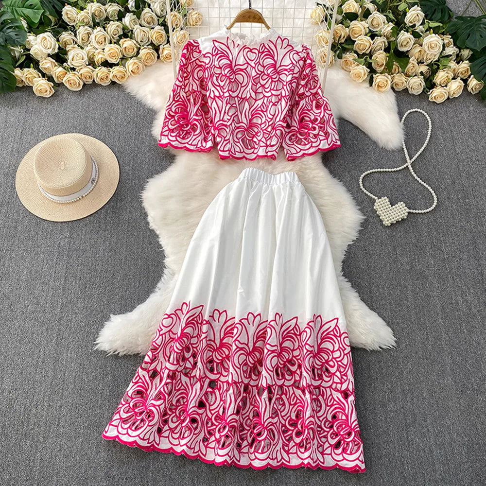 Pink and white embroidered top and skirt set on a gray surface with flowers and a hat.