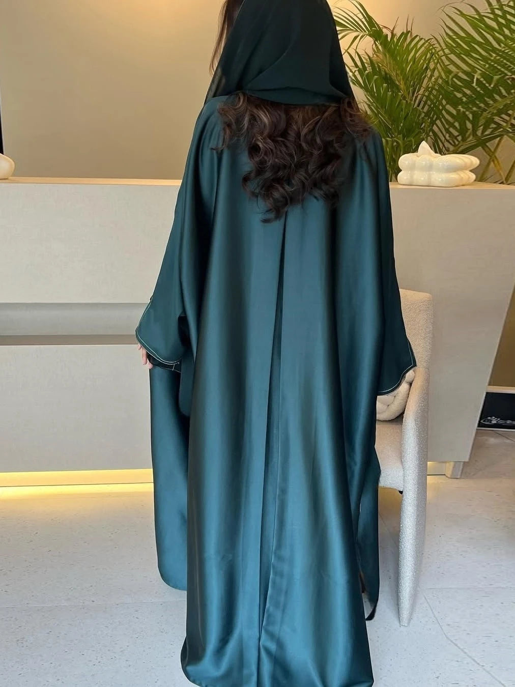 Person wearing a teal abaya in an indoor setting with a neutral background