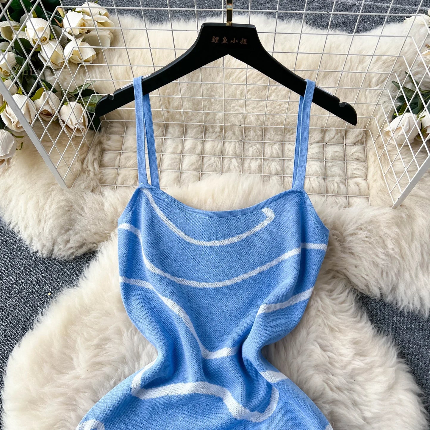 Blue knitted dress with white patterns on a hanger against a textured white and gray background.