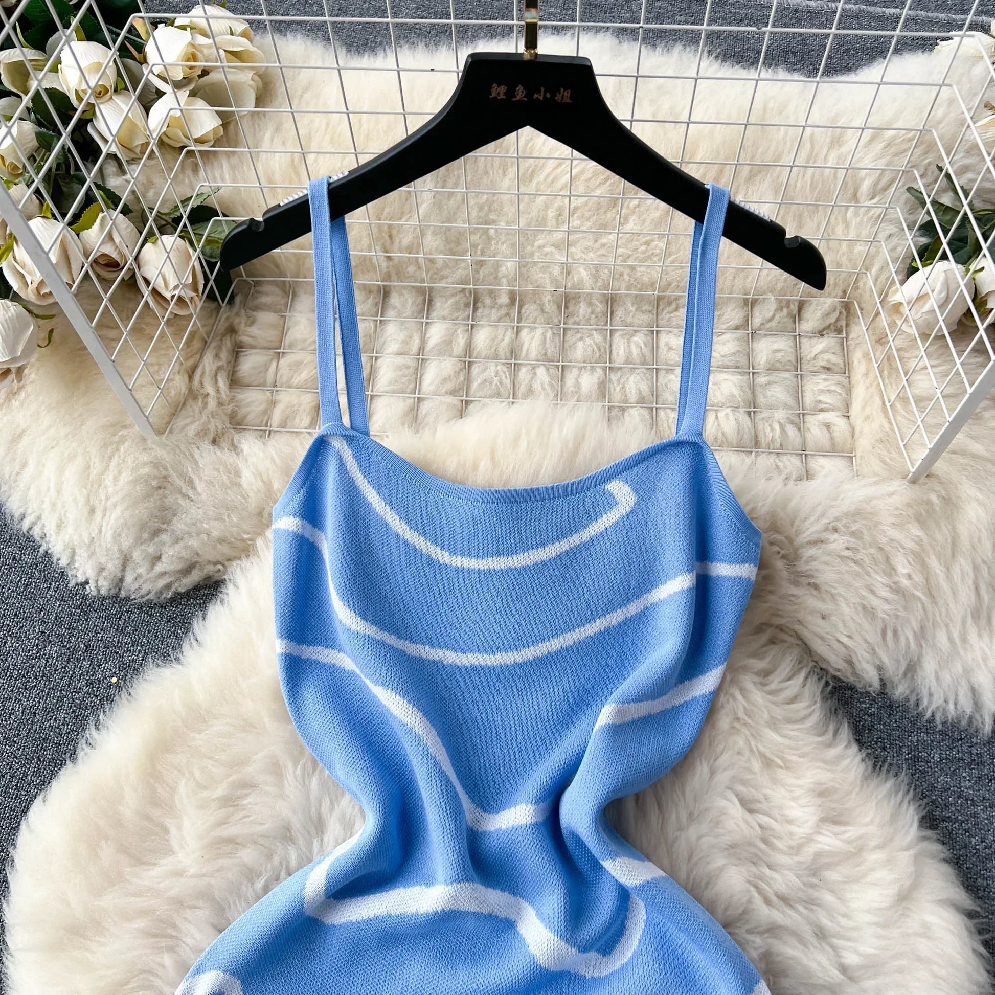 Blue knitted dress with white patterns on a hanger against a textured white and gray background.