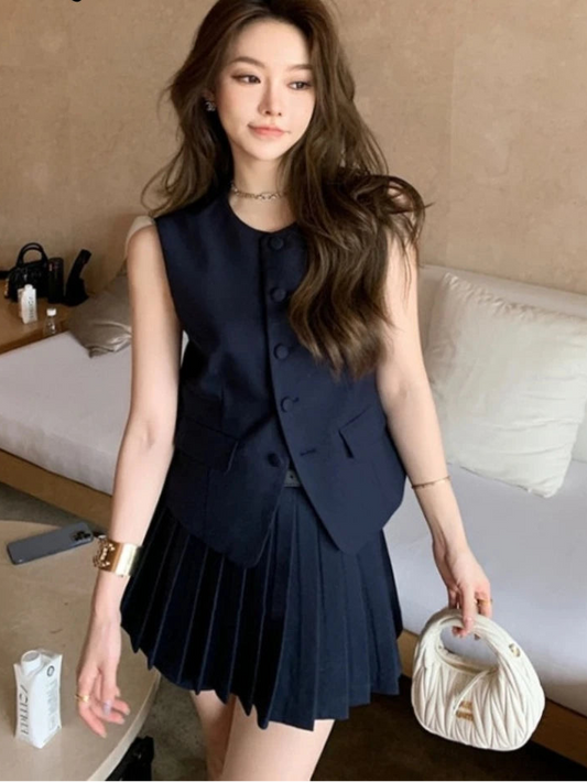 Woman wearing a navy blue pleated dress holding a white handbag in an indoor setting.