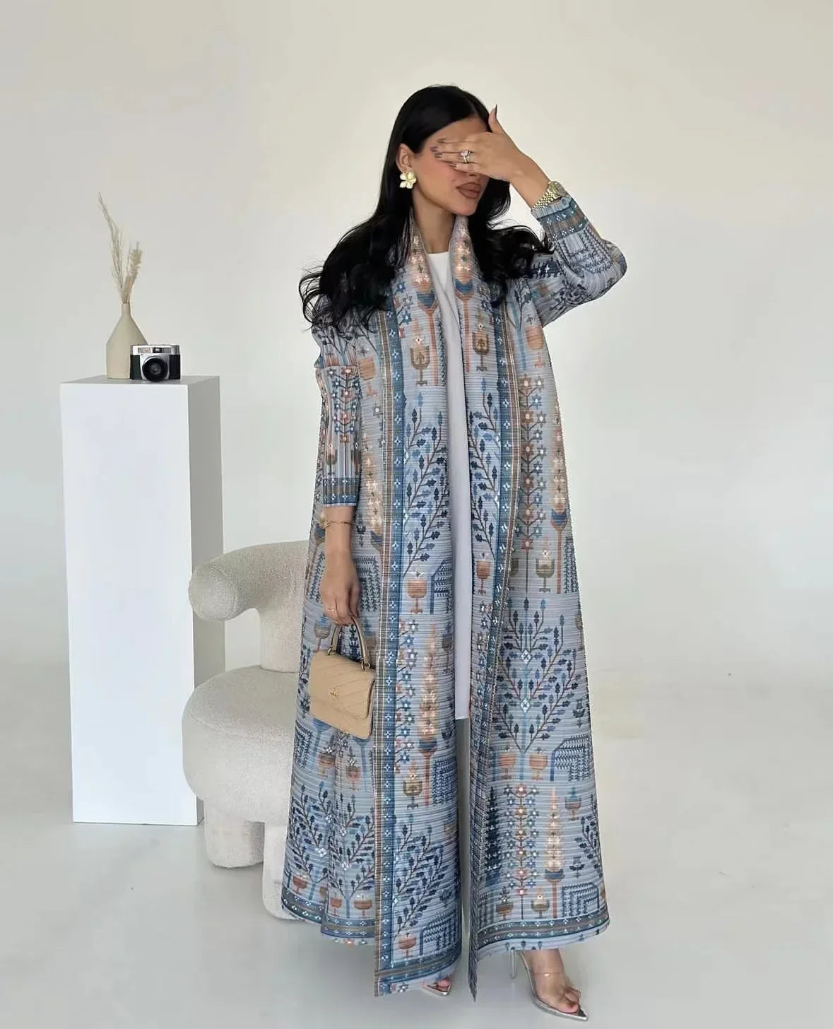 Woman wearing a long, patterned dress in a minimal white room.