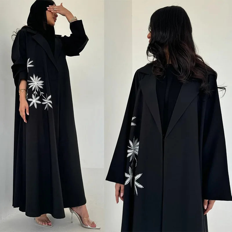 Black coat with white floral embroidery worn by a model on a plain background