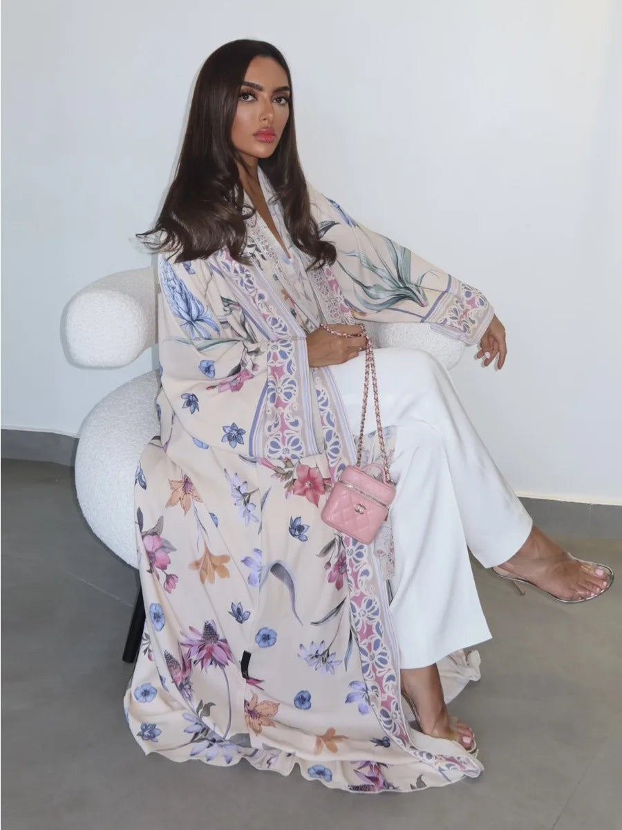 Woman sitting on a white chair wearing a floral dress and holding a pink handbag.