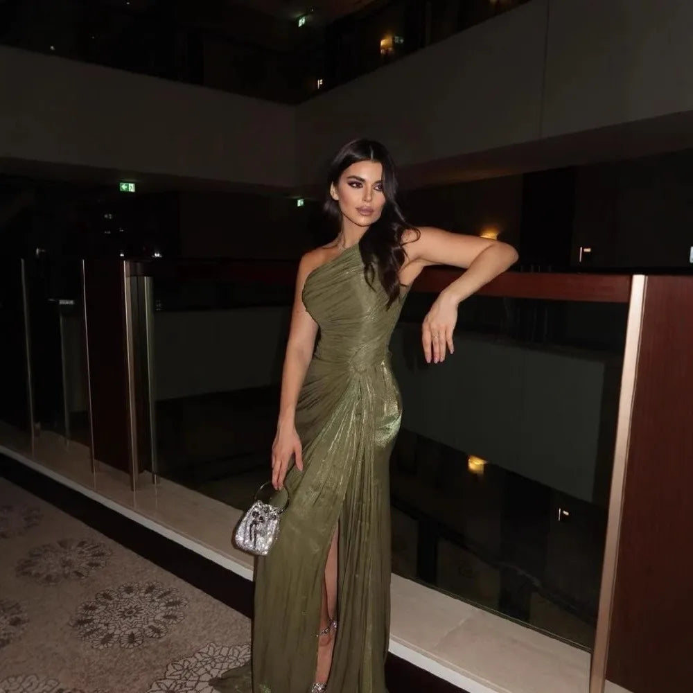 Woman in a green evening gown standing indoors with a dark background