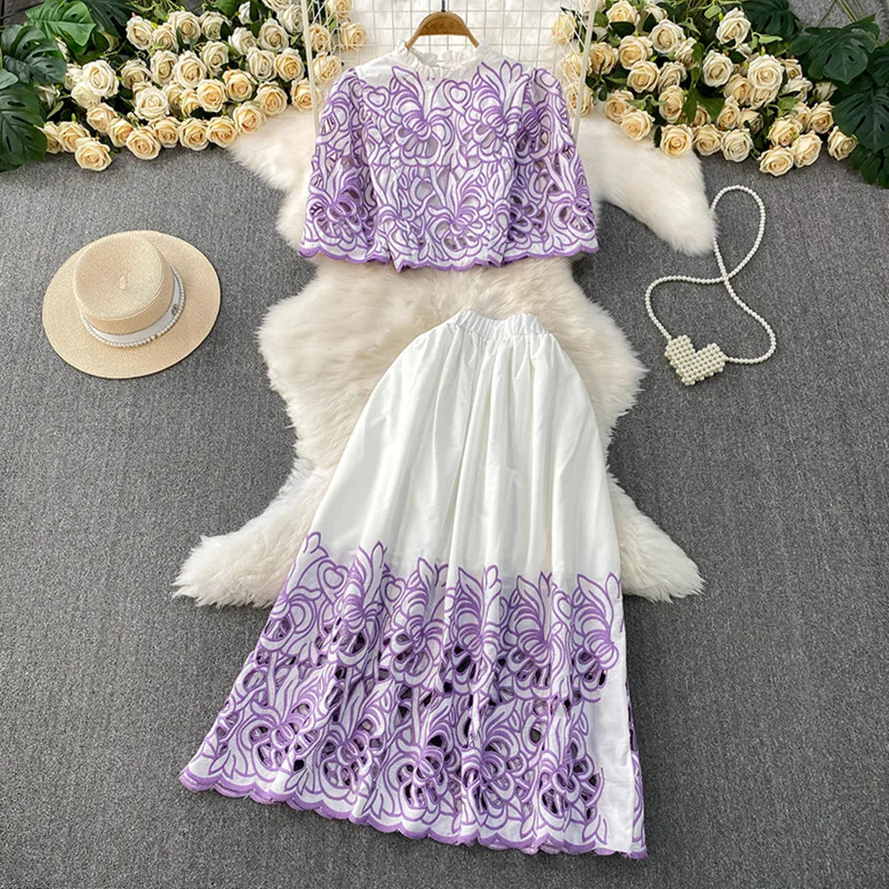 Purple and white embroidered top and skirt set with a hat and necklace on a gray surface.