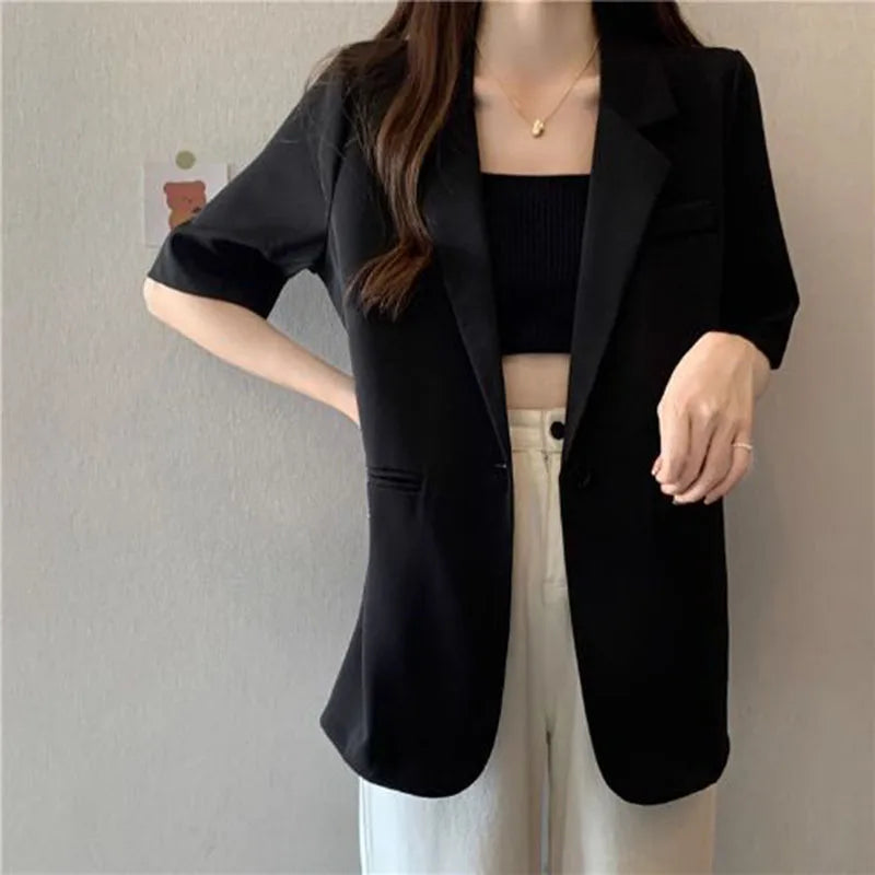 Person wearing a black blazer over a black top and white pants against a neutral background