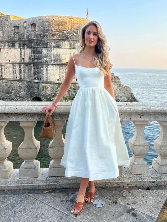 Woman in a white dress standing on a balcony with a scenic view of water and buildings.
