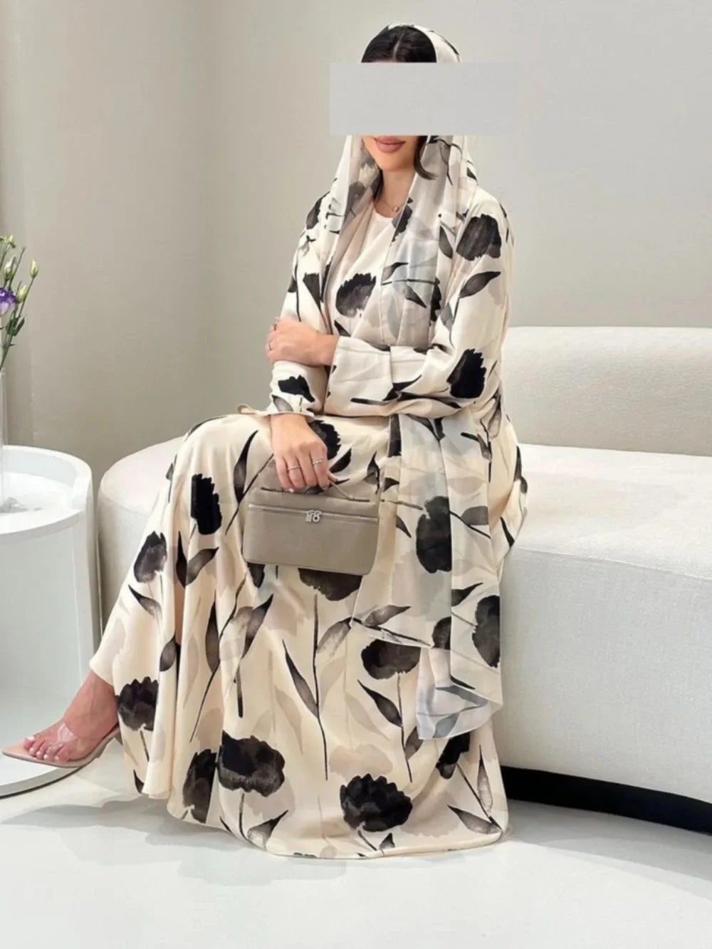 Woman wearing a long floral dress sitting on a white couch.