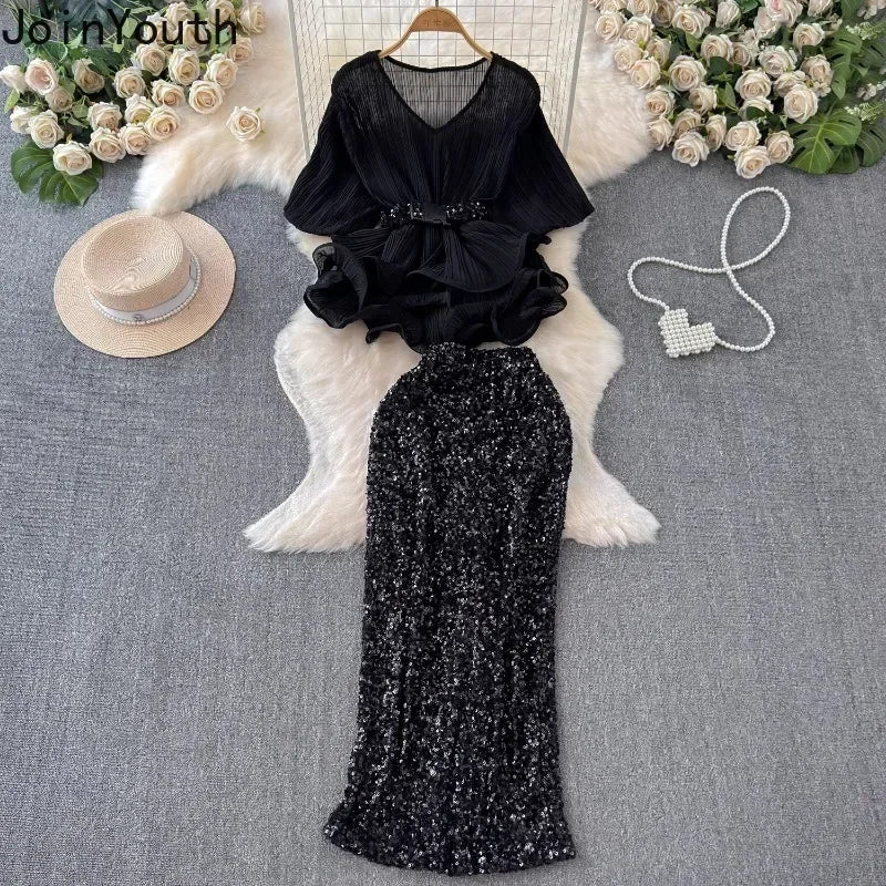 Black outfit with a top and sequin skirt on a textured surface with decorative elements.