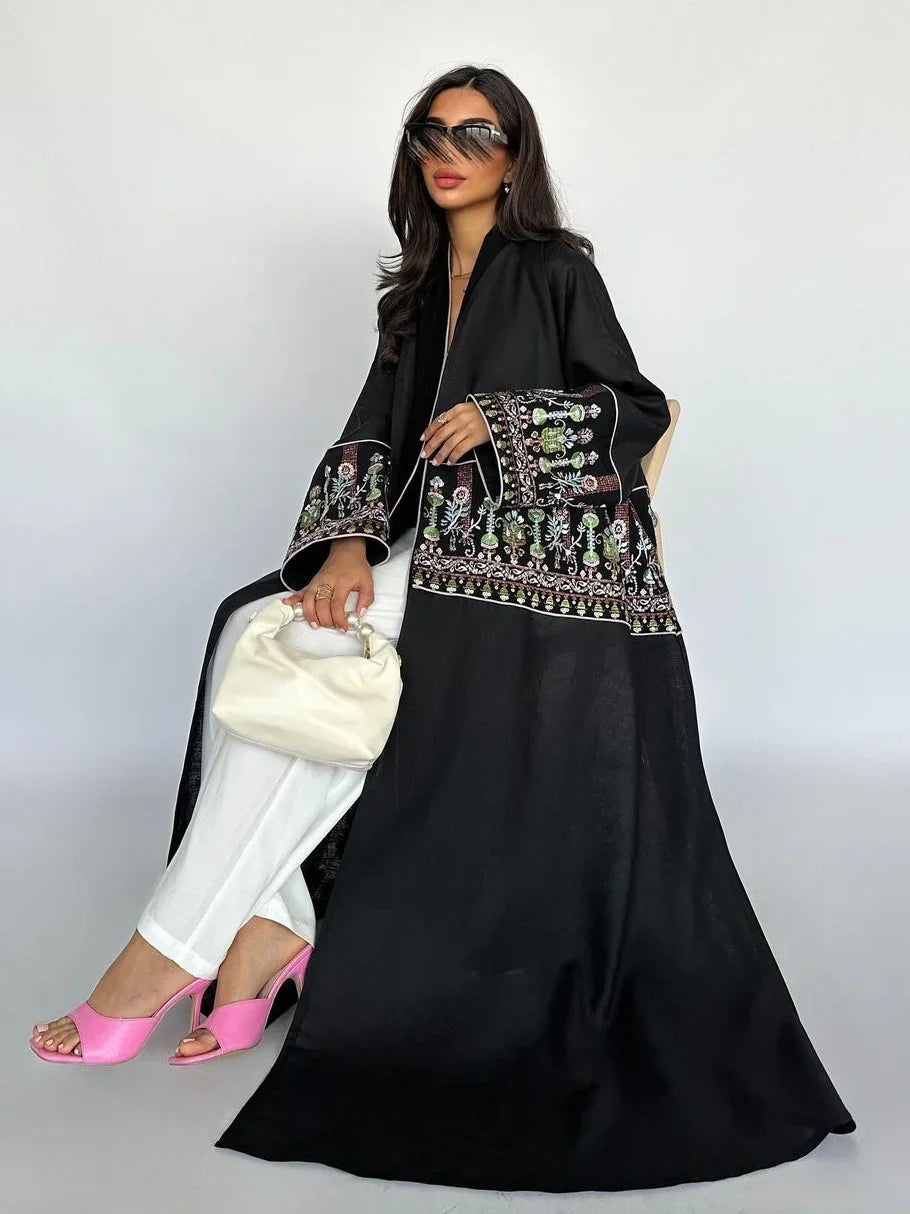 Woman wearing a black embroidered outfit with white pants and pink shoes, holding a white handbag.
