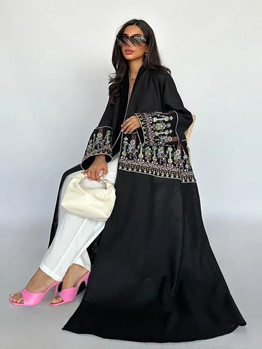 Woman wearing a black embroidered outfit with white pants and pink shoes, holding a white handbag.