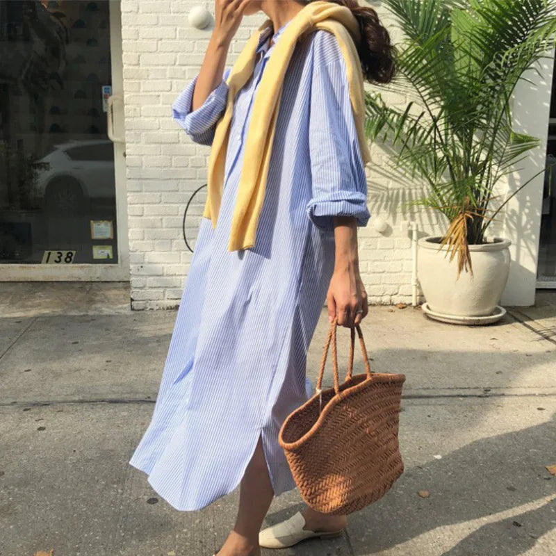 Person wearing a light blue striped shirt and holding a woven bag on a sidewalk.