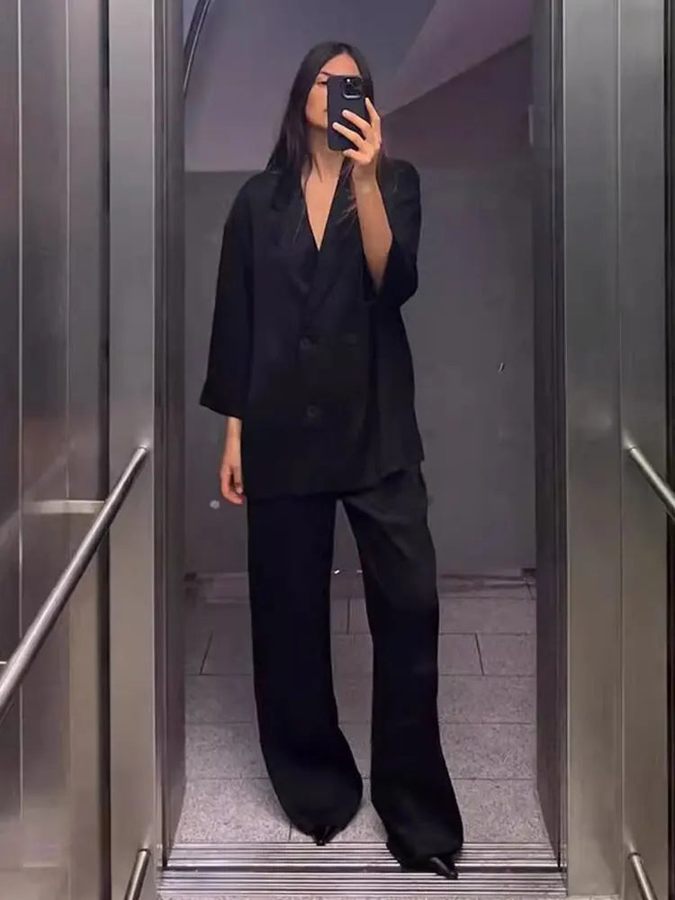 Person wearing a black outfit taking a mirror selfie in an elevator.