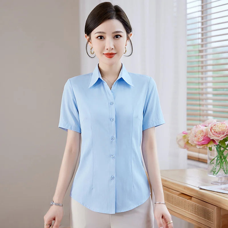 Woman wearing a light blue short-sleeve shirt in a room with a desk and flowers.