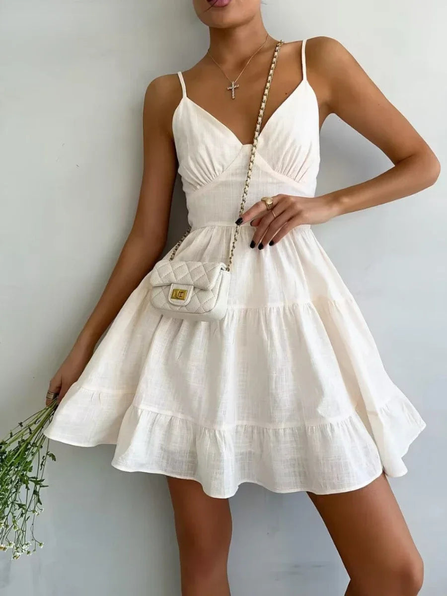 Woman wearing a white dress holding a small handbag against a plain background
