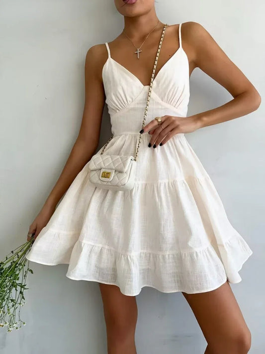 Woman wearing a white dress holding a small handbag against a plain background