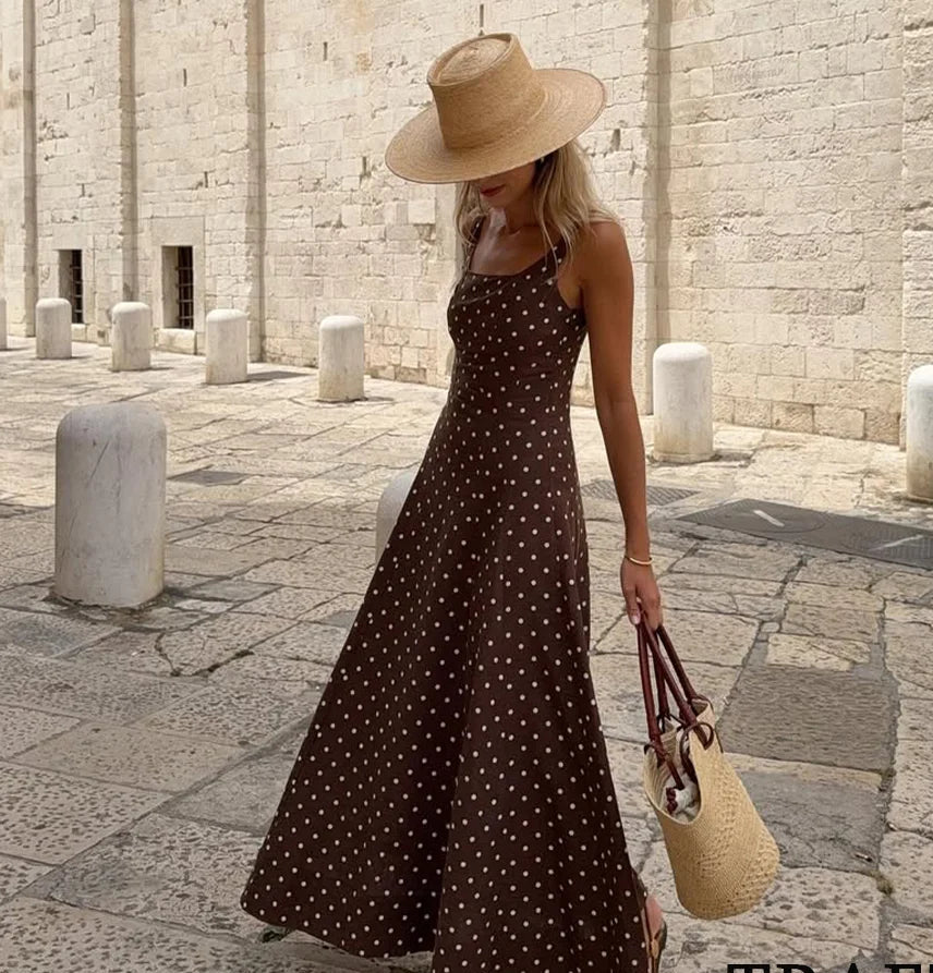Woman in a polka dot dress and straw hat standing on a stone pavement with 'Trafza' branding.