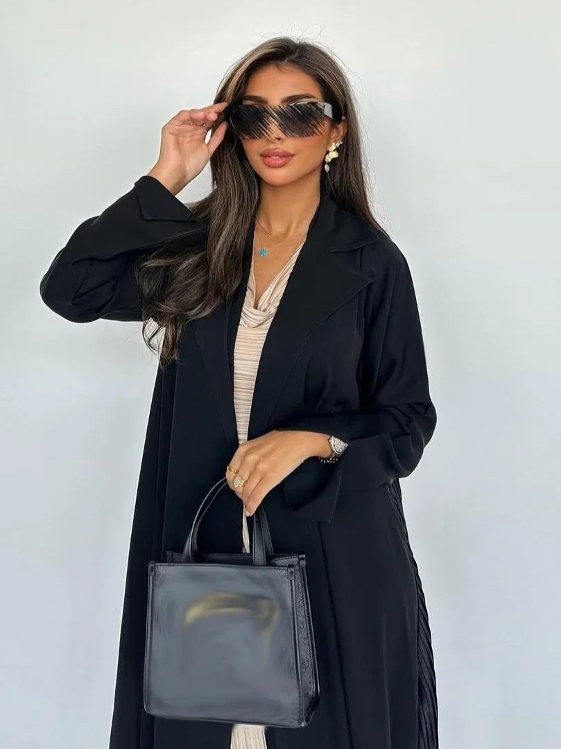 Woman in a black coat holding a black handbag against a white background