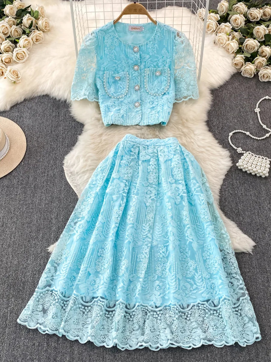 Light blue lace dress and cardigan set on a textured surface with flowers and a handbag.