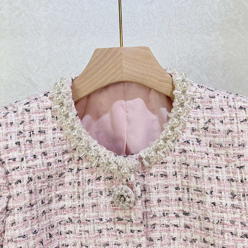 Pink tweed jacket with pearl collar on a wooden hanger against a light background