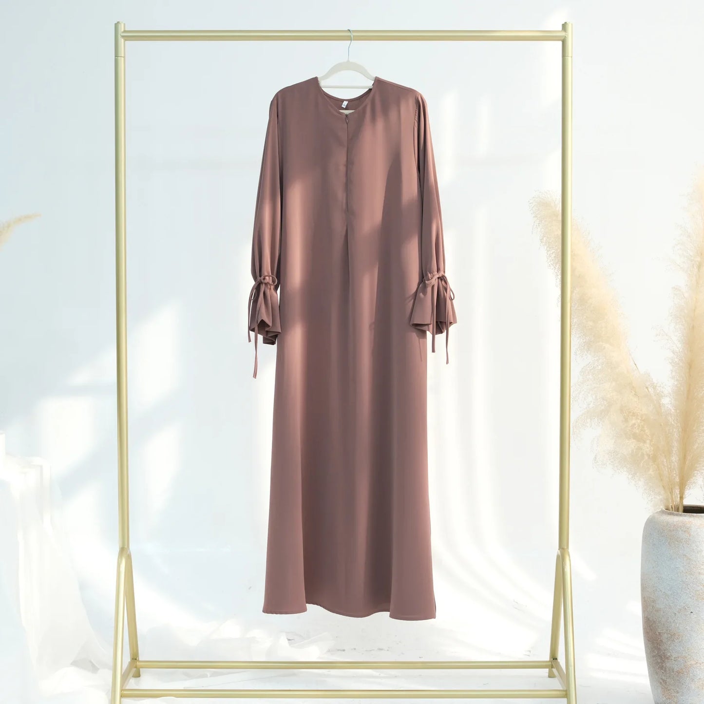 Brown dress hanging on a gold rack with a white background